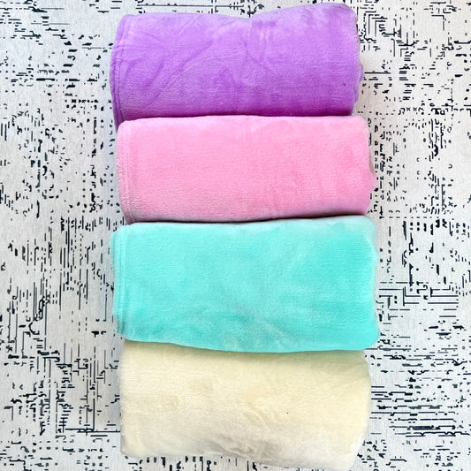4 plush blankets rolled up, and placed in a line. From top to bottom: Lilac, Pink, Teal, Cream.