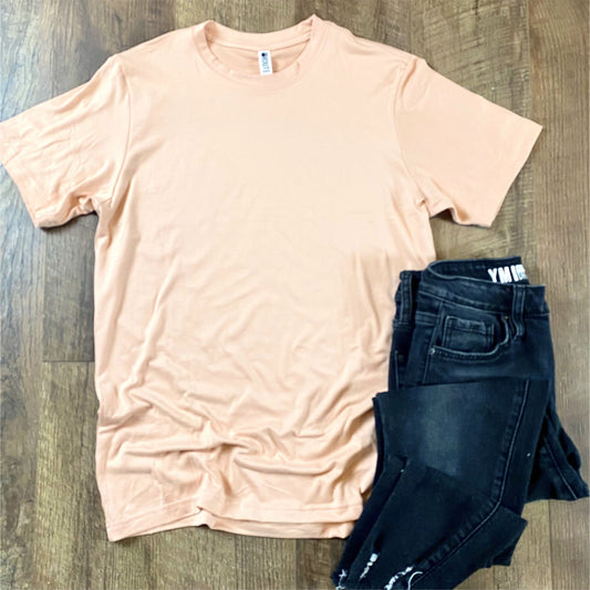Peach t-shirt laying flat on a hardwood floor background, pair of black jeans folded in corner