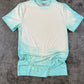 Aqua blue t-shirt with bleached front chest area, laying flat on a concrete background
